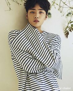 a young man with black and white striped shirt leaning against a wall