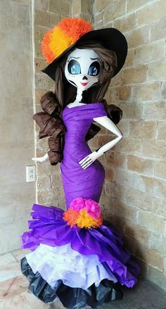 a doll is dressed in a purple dress and orange flower headband, standing next to a brick wall