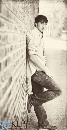 a young man leaning against a brick wall