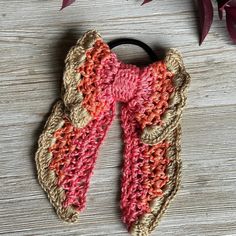 a crocheted scarf hanging on a wooden table next to a plant with leaves