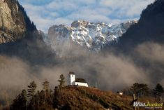 a church on a hill with snow covered mountains in the background and clouds rolling over it