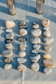 several rocks with names written on them sitting next to two cups and one candle holder