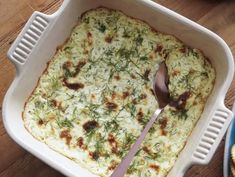 a casserole dish with cheese and herbs in it on a wooden table next to some crackers