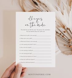 a hand holding up a printable wedding game with feathers on the table behind it