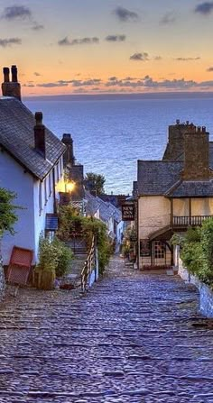 an old cobblestone street leading up to the ocean at sunset or dawn in england