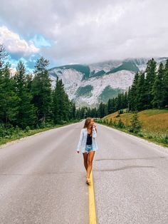 a woman is walking down the middle of an empty road in front of some mountains