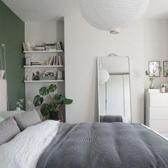 a bedroom with green walls and white bedding in the corner, along with a large mirror on the wall