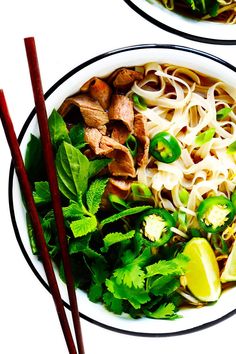 two plates filled with noodles, meat and veggies next to chopsticks