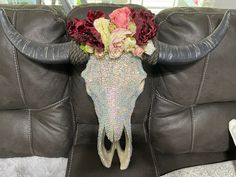 a cow skull with flowers on it's head sitting on a leather couch in a living room