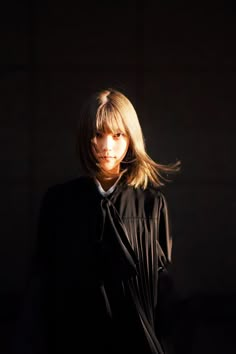 a woman standing in the dark with her hair blowing back and looking at the camera