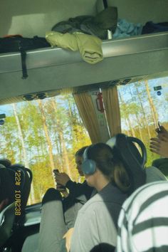 people sitting in the back of a bus looking at their cell phones while wearing headphones