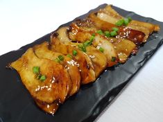 a black plate topped with meat covered in sauce and green onions