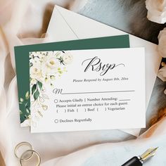 wedding rsp card with white flowers and greenery on it next to a fountain pen