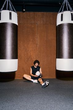 a man sitting on the ground in front of two large punching bags