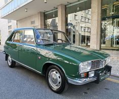 an old green car parked in front of a building