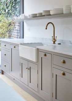 a kitchen with white cabinets and gold faucets on the counter tops, along with plates