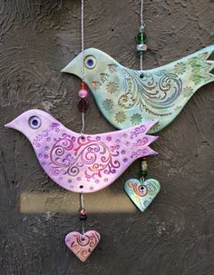 two colorful birds hanging on a wall with heart shaped ornaments attached to the back of them