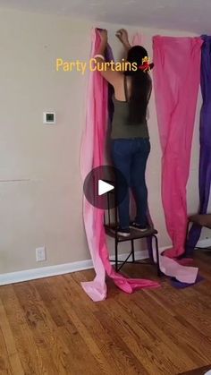 a woman standing on a chair in front of pink curtains