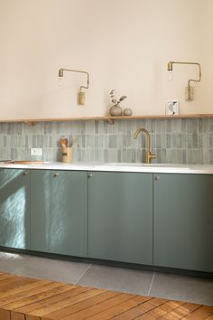 a kitchen with blue cabinets and wood flooring next to a counter that has gold faucets on it