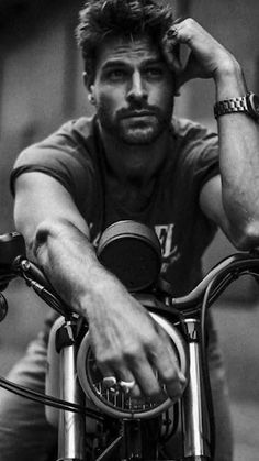 a black and white photo of a man sitting on a motorcycle with his hand on the handlebars