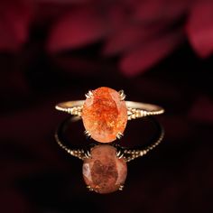 an orange ring sitting on top of a black surface with flowers in the back ground