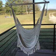 a white hammock hanging from the side of a wooden deck with trees in the background