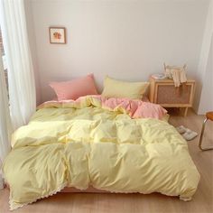 a bed with yellow and pink comforters in a room next to a window,