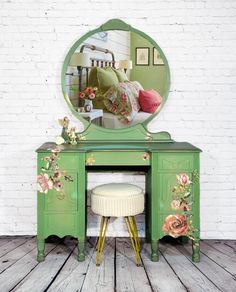 a green dresser with a mirror and stool in front of it on a wooden floor