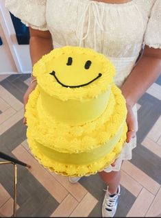 a woman holding a yellow cake with a smiley face on it