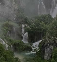 a waterfall in the middle of a forest filled with lots of green trees and water