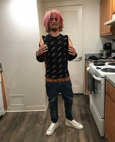 a man with pink hair and dreadlocks standing in a kitchen next to an oven