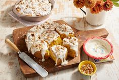 a wooden cutting board topped with a cake next to a bowl of whipped cream and flowers