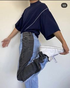 a man holding a pair of white shoes in his right hand while standing against a wall