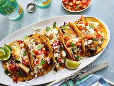 three tacos on a plate with limes and salsa