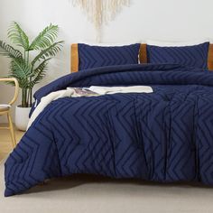 a bed with blue comforter and pillows in a room next to a potted plant