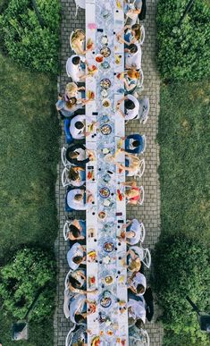 an overhead view of a long table with people sitting at it outside in the grass