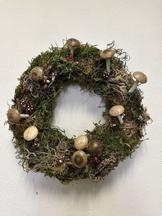 a moss wreath with mushrooms and berries is hanging on the wall in front of a white wall