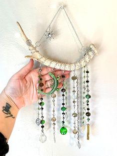 a hand holding a necklace with beads and charms hanging from it's side on a white wall