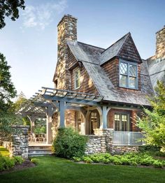 a stone house with a porch and covered in wood shingles, surrounded by lush green grass