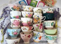 a pile of tea cups and saucers on a doily with lavenders in the background