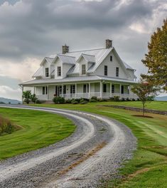 a large white house sitting on top of a lush green field next to a dirt road