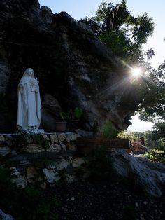 there is a statue on the side of a hill with trees in the background and sun shining through