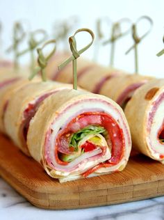 a wooden cutting board topped with cut in half ham and cheese roll sandwiches on skewers