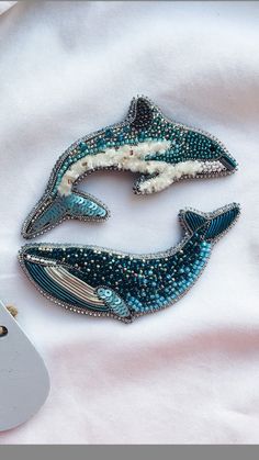 two blue and white whale brooches sitting on top of a white sheet next to a computer mouse