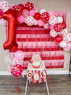 a red and white birthday party with balloons, streamers and cake on a chair