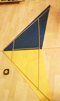 a blue and yellow kite sitting on top of a wooden floor next to a laptop computer