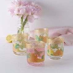 four glass cups sitting on top of a table next to a vase filled with flowers