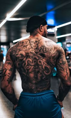 a man with tattoos on his back standing in a gym