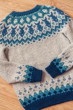 a blue and white sweater with matching mittens sits on a wooden floor next to a pair of scissors