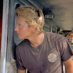 a young man with blonde hair standing in front of a door and looking at something